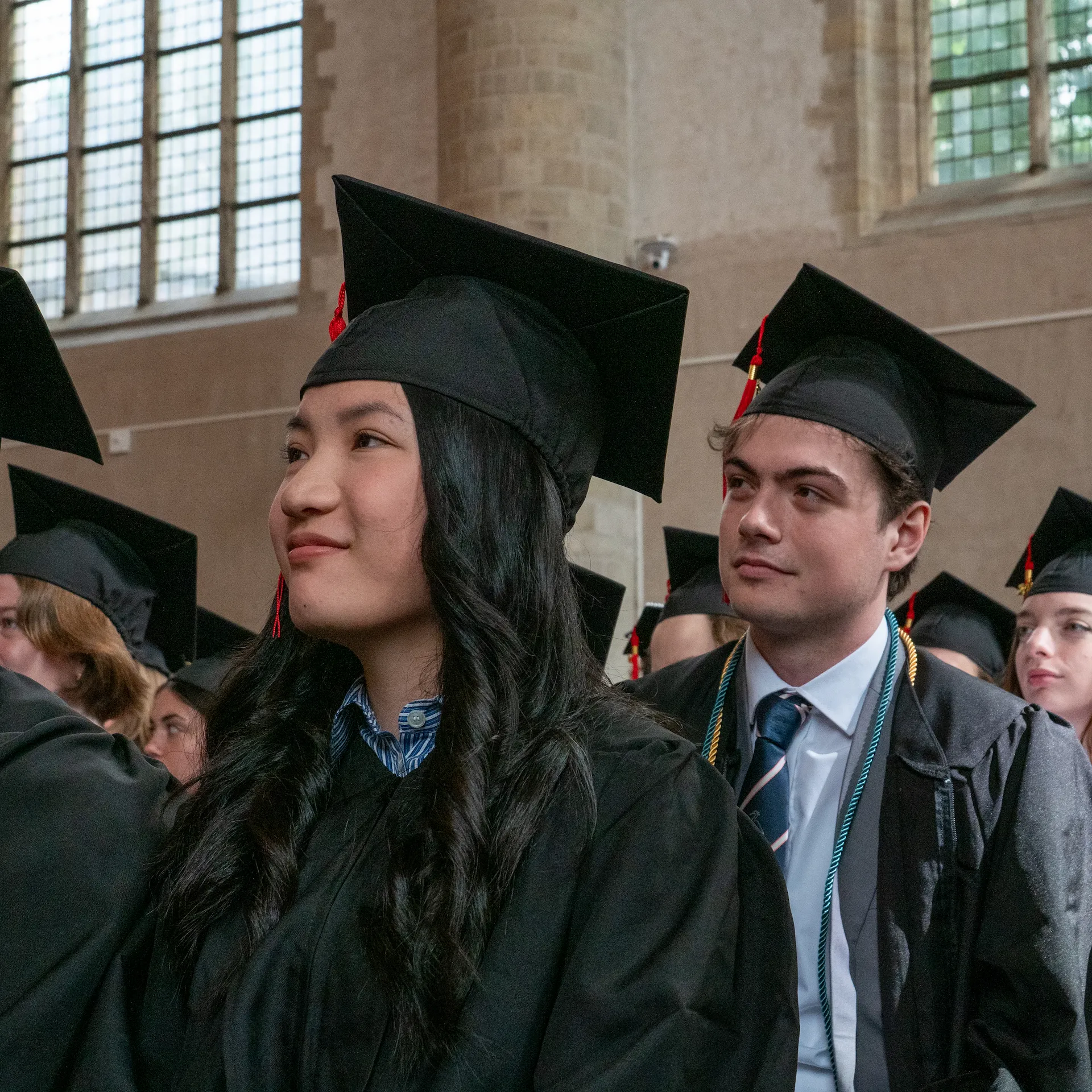 Two college students seated at graduation looking forward with a soft smile on their faces